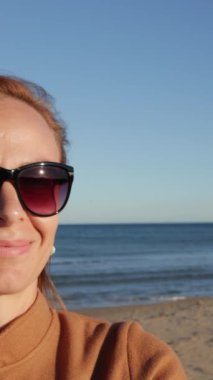 Denizin arka planında güneş gözlüklü genç bir kadın