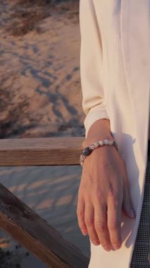 İskelede beyaz bir gelinlik tutan bir kadının ellerini yakın çekim.