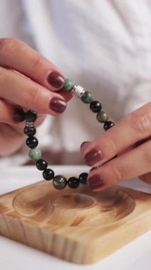 Siyah manikürlü kadın elleri yuvarlak bir kolye tutuyor.