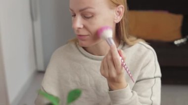 Evde makyaj yapan bir kadın sabah güzellik tedavisi yapıyor. Kız makyaj için kozmetik fırça kullanıyor.