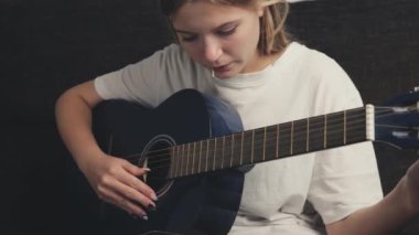 Genç kız evde akustik gitar çalıyor.