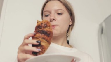 Kadın elinde çikolatayla kruvasan yiyor.