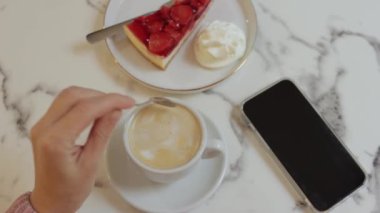 Kadın akıllı telefonuyla bir fincan kahve ve kek alıyor.