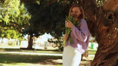 Bir buket çiçek tutan bir kadın, açık havada.