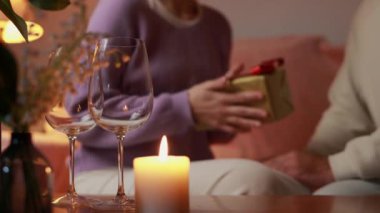 Evdeki masada hediye kutusu ve bir bardak şampanyası olan genç çift.