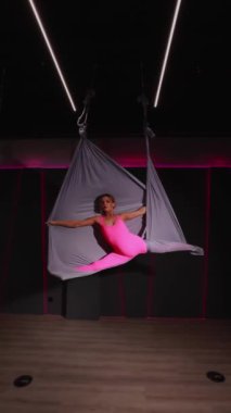 Stüdyoda pembe ipek elbiseli ve siyah takım elbiseli bir kadın var.