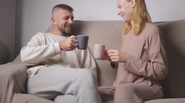 Evdeki kanepede oturup kameraya bakan mutlu bir adam ve kadın.