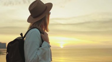 Gün batımında sırt çantalı genç bir kadın gezgin. Şapkalı ve sırt çantalı bir gezgin. Dünyaya seyahat et..