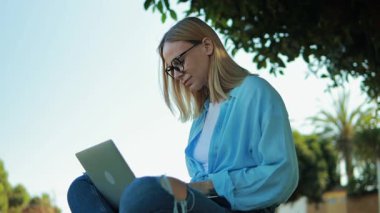 Genç kız güneşli bir yaz gününde sokakta dizüstü bilgisayar kullanıyor.