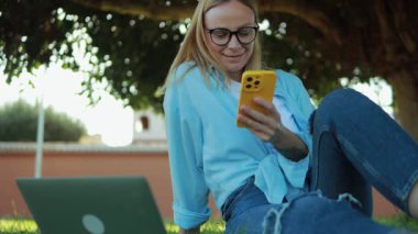 Gözlüklü ve sarı kazaklı genç bir kız parkta oturur ve bir mesaj okur..