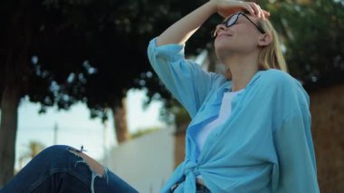 Mavi kot elbiseli kız bankta oturuyor ve gülümsüyor..