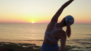 Genç bir kadın plajda yoga egzersizi yapıyor.