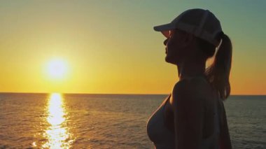 Genç bir kadın deniz sahilinde günbatımının tadını çıkarıyor.