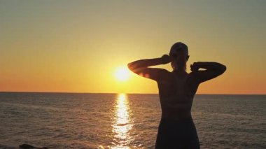 Silüet genç kadın deniz sahilinde esneme egzersizi yapıyor.