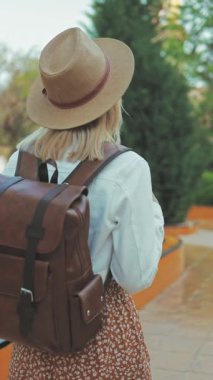 Sırt çantalı, şapkalı güzel bir kız parkta yürüyor.