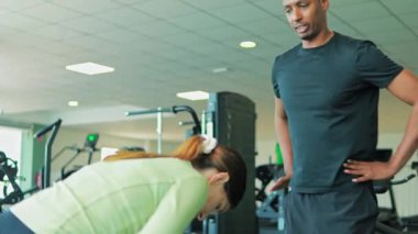 Spor salonunda dambıllarla egzersiz yapan bir adam.