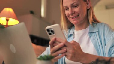 Evde akıllı telefon kullanan genç bir kadın.