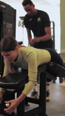 Genç bir kadın spor salonunda antrenörle egzersiz yapıyor.