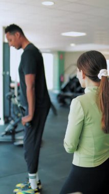 Formda bir kadın spor salonunda antrenörle egzersiz yapıyor..