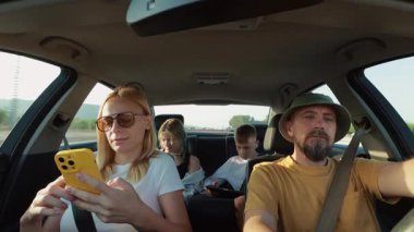 Akıllı telefonlu bir aile arabada selfie çekiyor.