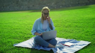 Yeşil çimenlikteki çimlerin üzerinde dizüstü bilgisayarı olan güzel bir kadın.