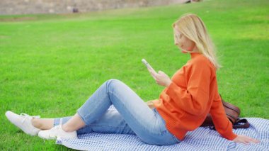 Cep telefonlu genç bir kadın parkta oturuyor.