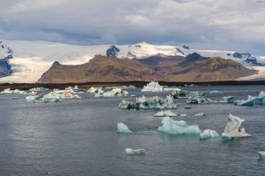 JkulsrIn İzlanda 'daki buzul gölünde, suda mavi buzdağları ve arka planda dağları vardı.