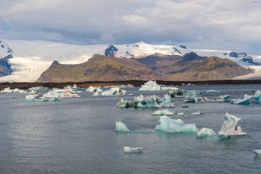 JkulsrIn İzlanda 'daki buzul gölünde, suda mavi buzdağları ve arka planda dağları vardı.