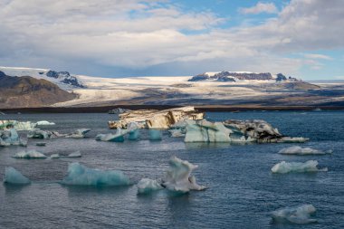 JkulsrIn İzlanda 'daki buzul gölünde, suda mavi buzdağları ve arka planda dağları vardı.