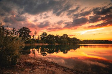 Gün batımından sonra bir orman gölünde dramatik bir alacakaranlık. Gölde yansıtılan güzel gün batımı.