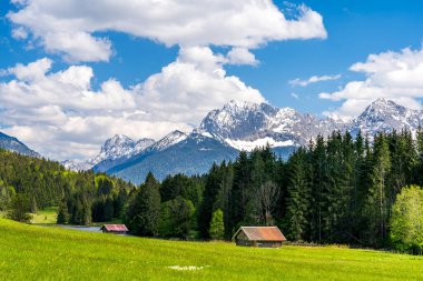 Almanya 'nın Bavyera kentindeki Geroldsee ve Karwendel Dağları' na bakan ahşap kulübeleri olan dağlık bir çayır.
