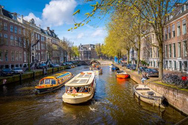 Amsterdam 'da klasik bir kanal sahnesi. Renkli, tarihi Hollanda binalarının yanından geçen bir yolcu gemisi.