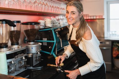 Kahve makinesiyle kahve hazırlayan profesyonel sarışın barista. Genç bayan kahve yapıyor.