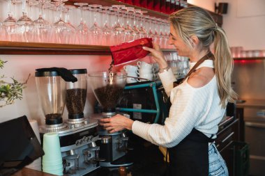 Kahve makinesiyle kahve hazırlayan profesyonel sarışın barista. Genç bayan kahve yapıyor.