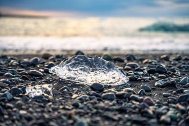 İzlanda 'da kışın bulutlu gökyüzüne karşı deniz kıyısındaki ıslak kayalar üzerinde kristal şeffaf buz kütlesi