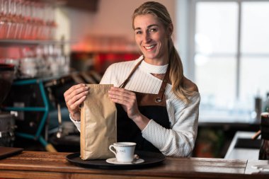 Barda çalışırken kahve servisi yapan gülümseyen barmen.