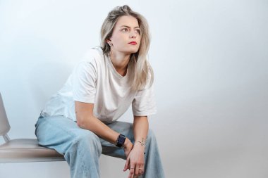 Beyaz tişörtlü, uzun sarı saçlı ve kot pantolonlu beyaz bir arka planda izole edilmiş bir Alman kızın portresi.