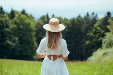 Sarışın bir kadının hasır şapka giydiği ve beyaz bir yaz elbisesi giydiği arka manzara. Doğada güzel bir kadın. Yaz havası.