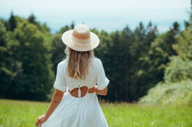 Sarışın bir kadının hasır şapka giydiği ve beyaz bir yaz elbisesi giydiği arka manzara. Doğada güzel bir kadın. Yaz havası.
