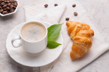 Kahve bardağı, kavrulmuş kahve çekirdekleri ve beyaz masada ekmek.