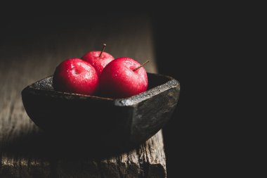 Ahşap kabın içindeki küçük erik yığınları, siyah arkaplanda.