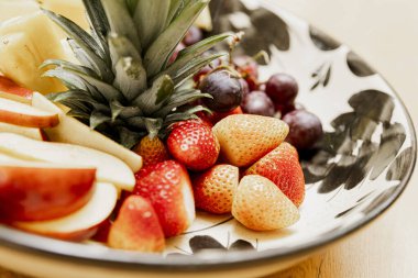 A closeup shot of a fruit platter with sliced pineapple, strawberries, and grapes. The platter is made of white ceramic with black accents. clipart