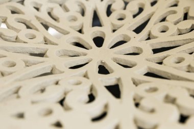 Yüzeyine karmaşık bir çiçek deseni oyulmuş beyaz bir masa kapağı. Tasarım, daha küçük ve karmaşık desenlerle çevrili, simetrik yapraklı merkezi bir çiçeğe sahiptir..