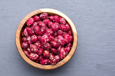 Kırmızı ve beyaz fasulyelerle dolu ahşap bir kase tahta bir yüzeyde duruyor. Fasulyeler tombul ve parlıyor, doğal, kırsal bir cazibesi var..