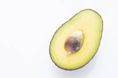 Kahverengi tohumu olan yarım avokado beyaz arka planda gösterilir. Avokado eti soluk sarı, ten de koyu yeşil ve biraz da kahverengi..