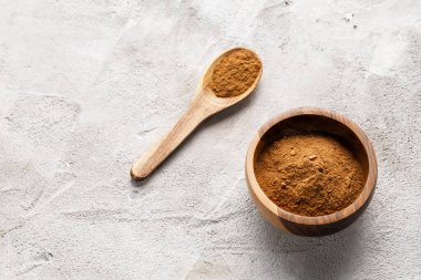 Zemin tarçınla dolu ahşap bir kase beyaz desenli arka planda iki tarçın çubuğunun yanında oturur..