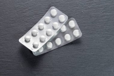 Birbiri ardına iki paket beyaz hap, siyah bir levha yüzeyinde yatıyor..
