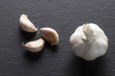 Sarımsak karanfillerinin yakın plan çekimi soyuldu ve siyah bir levhaya saçıldı. karanfiller soluk kahverengi ve beyazdır ve bazı pembe röfleleri vardır. Deriler de var, kısmen soyulmuş ve dağılmış.