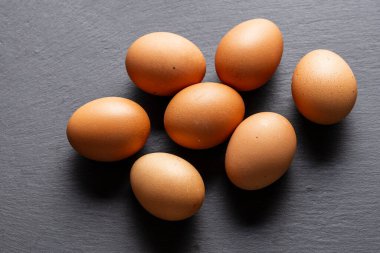 Gri bir levhaya saçılmış yedi kahverengi yumurta. Yumurtalar rastgele dizilmiş ve üst üste binmiş. Görüntü biraz daha yüksek bir açıdan alınır, yumurtaları tek bir açıdan gösterir.