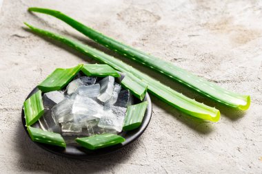 The image shows aloe vera leaves and aloe pulp in small pieces, on a light-colored background